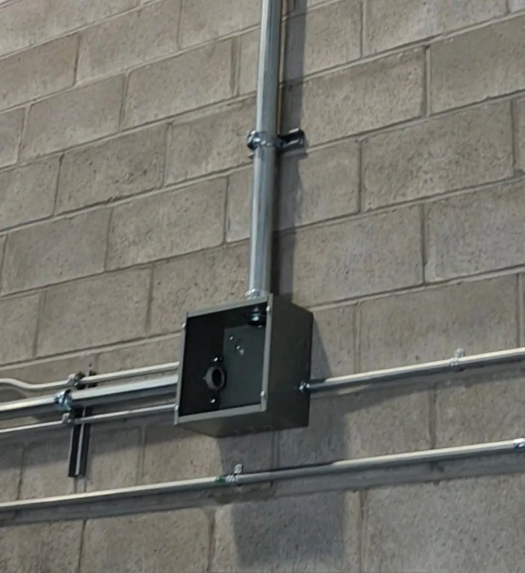 Conduits EMT alignés et boîte de jonction installés sur un mur de blocs de béton dans un local commercial
